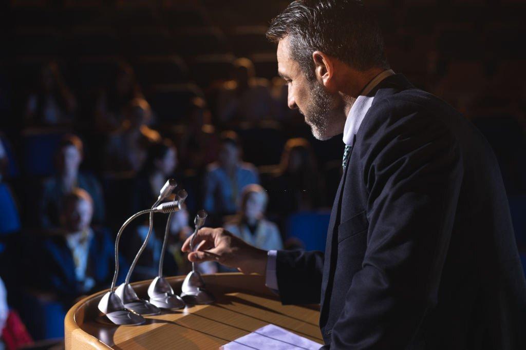 Side view of Caucasian businessman holding podium speaker in his hand at auditorium